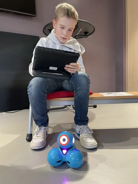 Junge arbeitet an Tablet, vor ihm ein Roboter aus blauen Kugeln