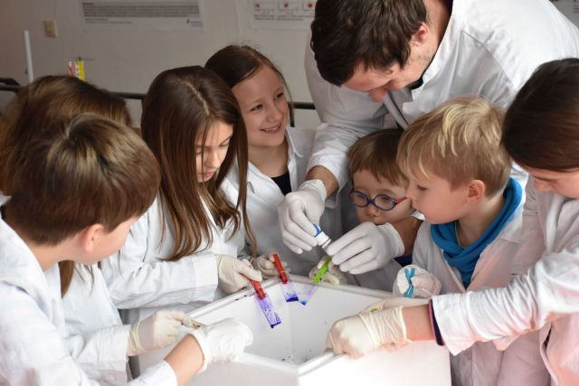 Kinder in Laborkitteln experimentieren unter Anleitung eines Erwachsenen